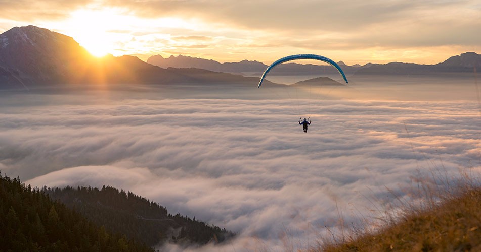 Person parachuting into clouds between mountains