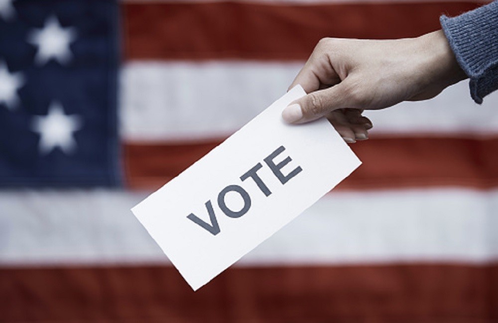 Picture of paper with 'vote' written on it with and American flag behind it 