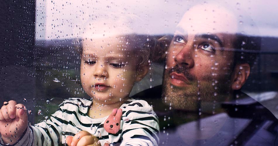 Father and child watching rain through window
