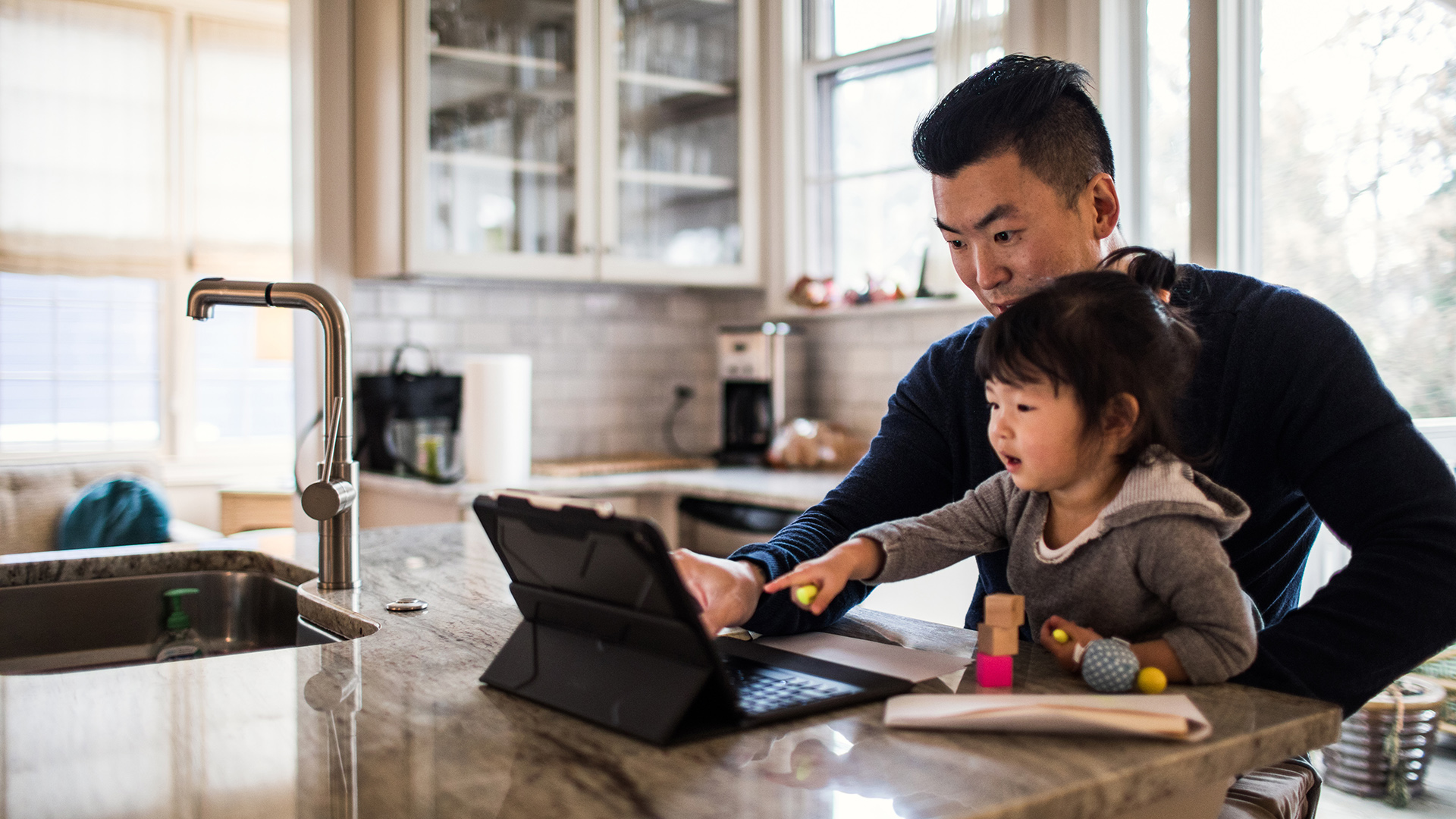 Father and child using tablet together in kitchen