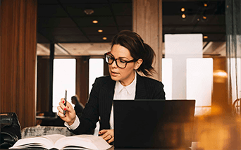 Lady looking at book and working on laptop
