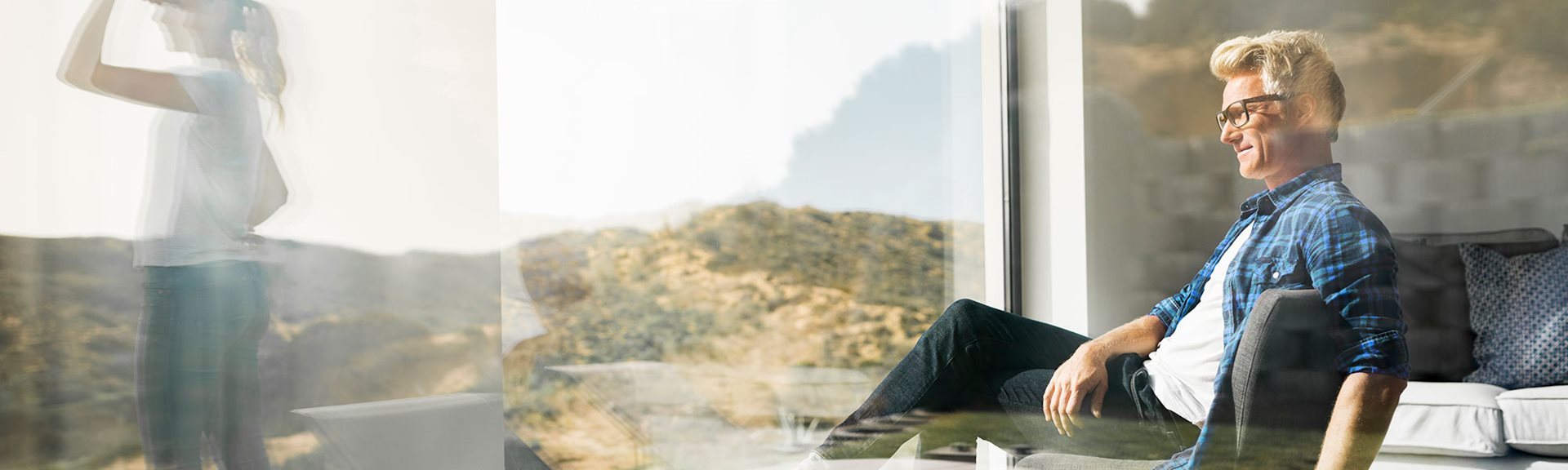 Man sitting in modern home with woman standing outside window