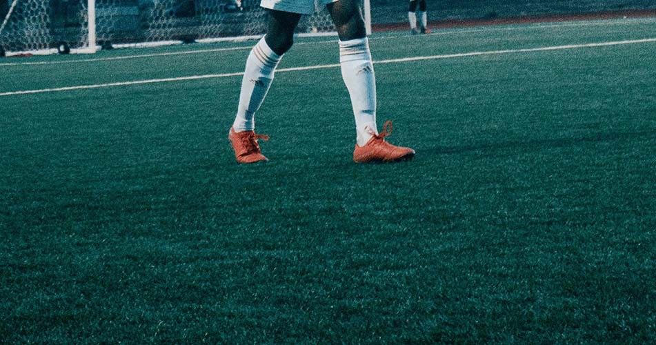 Footballer walking on pitch wearing orange football boots