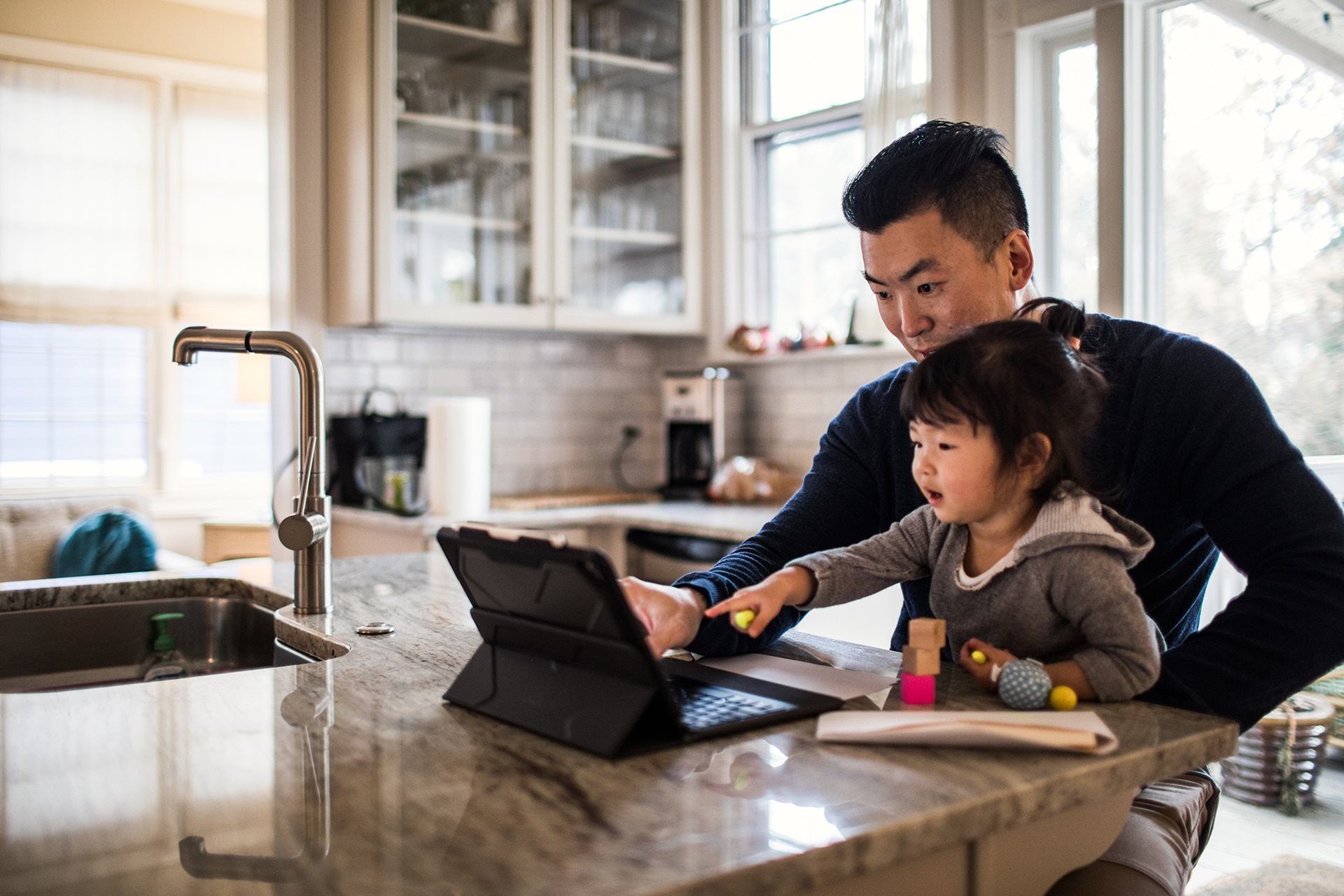 Father and child using tablet together in kitchen