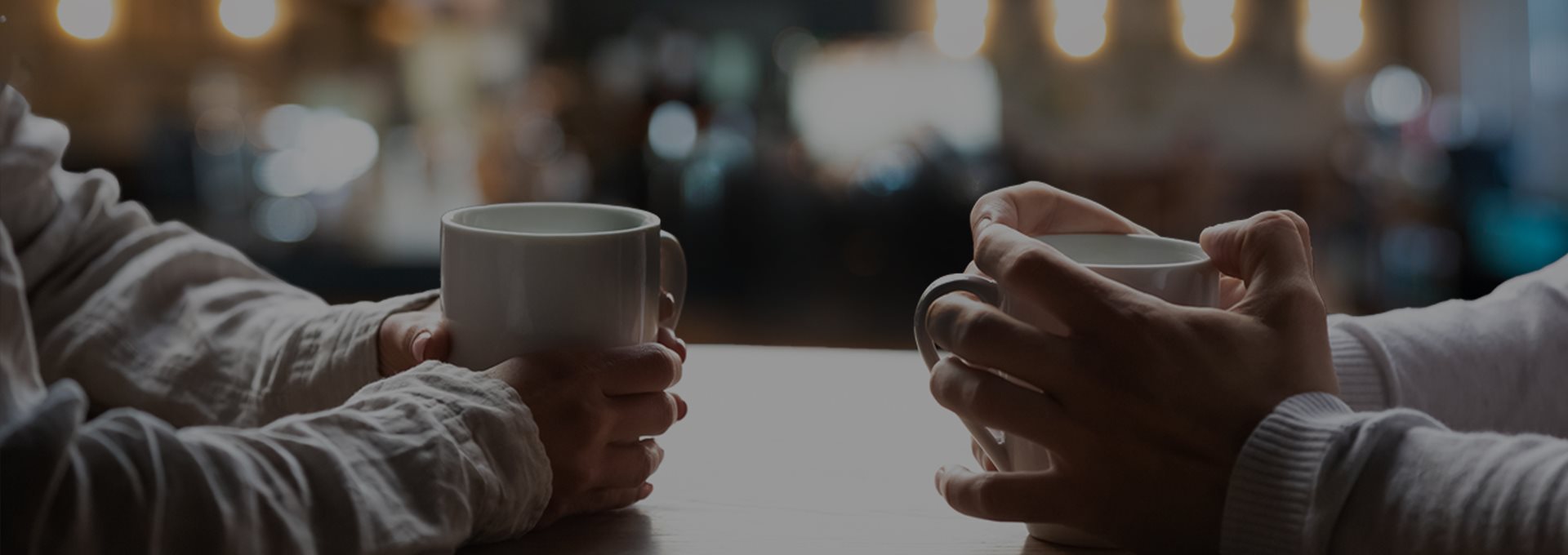 Two people sitting across a table holding coffee cups