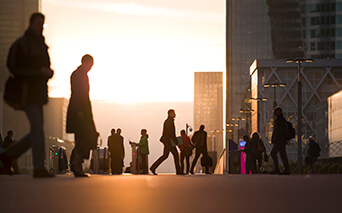 People walking in a city at sunrise/sunset with high-rise buildings in the background