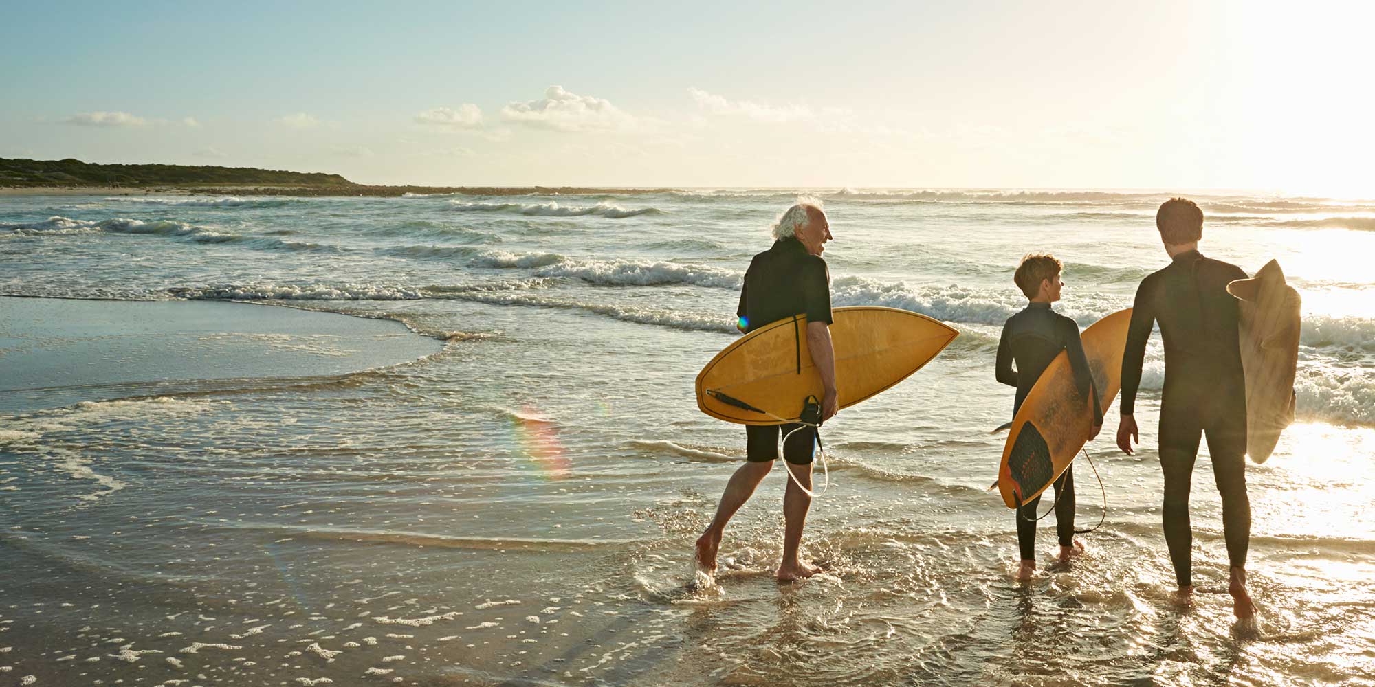 Family of three generations of surfers walking on the beach